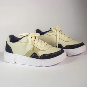 Par de tênis casual creme e azul marinho com cadarços bege e solado branco grosso em fundo claro.