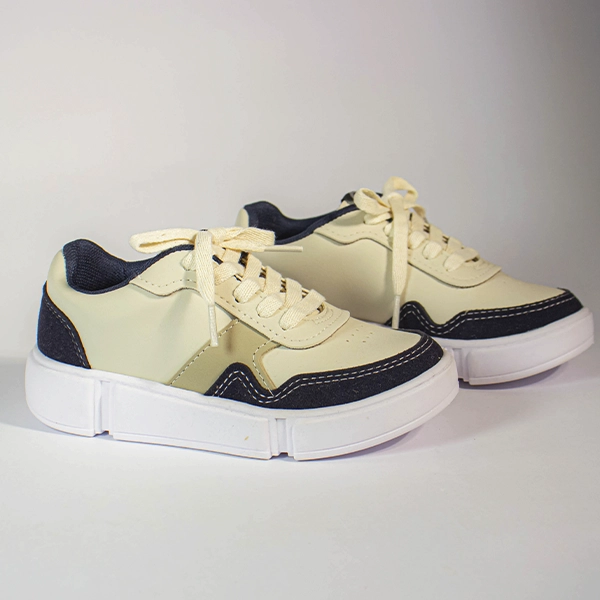 Par de tênis casual creme e azul marinho com cadarços bege e solado branco grosso em fundo claro.